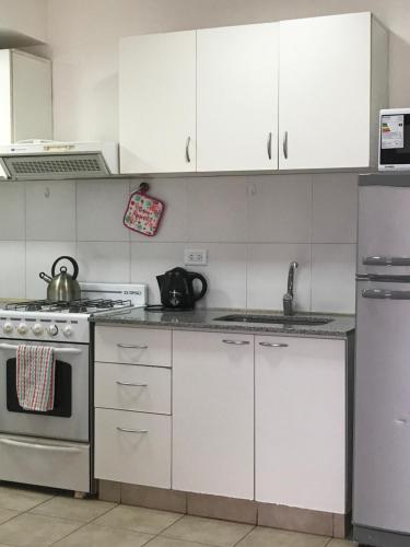 cocina con armarios blancos, fogones y nevera en Departamento Leloir Neuquén en Neuquén