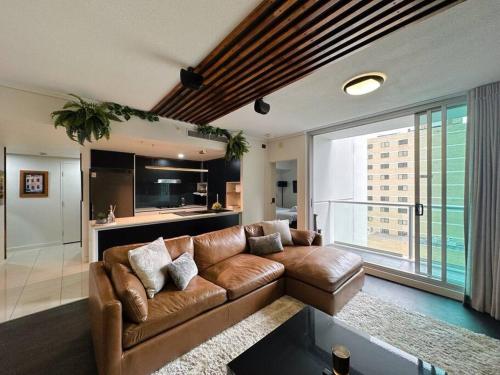 a living room with a brown leather couch and a kitchen at S&P Apartments - Festival in Brisbane
