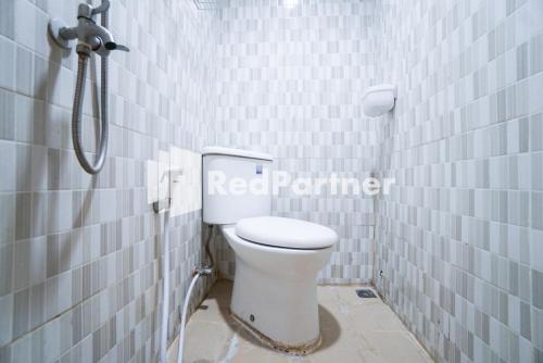 a bathroom with a toilet in a white tiled wall at Eascot Hotel Mitra RedDoorz in Jakarta