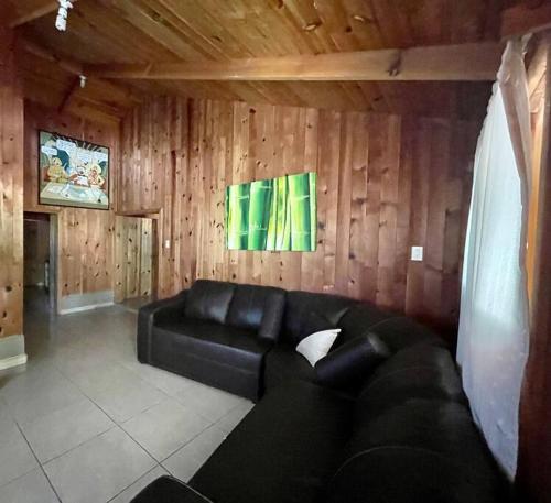 a living room with a black couch and wooden walls at Cómoda Cabaña El puchero ,Surutato, el Puchero in Surutato