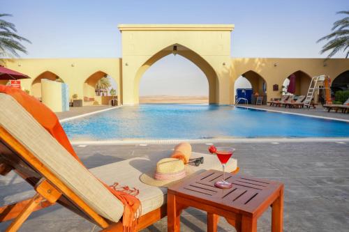 a pool with a chair and a table with a glass of wine at Tilal Liwa Desert Retreat in Madīnat Zāyid