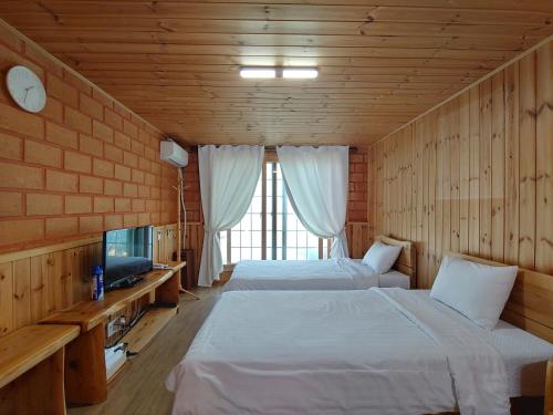 a bedroom with two beds and a tv and a window at Jeju Hanibaram Pension in Jeju