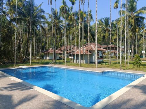 a swimming pool in front of a house with palm trees at Kalappura Farm House Heritage in Ottappālam
