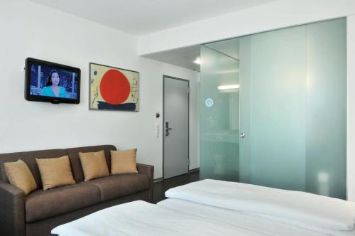 a bedroom with a bed and a couch and a tv at Sorell Hotel Ador in Bern