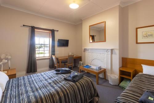 una camera d'albergo con letto, scrivania e finestra di The Victoria Hotel a Port MacDonnell