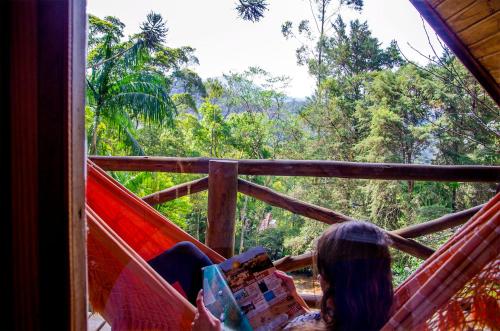 a woman sitting in a hammock looking out at the forest at Pousada Rancho Das Framboesas in Visconde De Maua