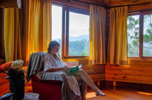 a woman sitting in a chair reading a book at Pousada Rancho Das Framboesas in Visconde De Maua