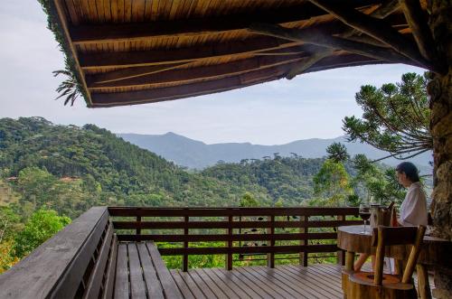 a man sitting at a table on a deck looking at the mountains at Pousada Rancho Das Framboesas in Visconde De Maua