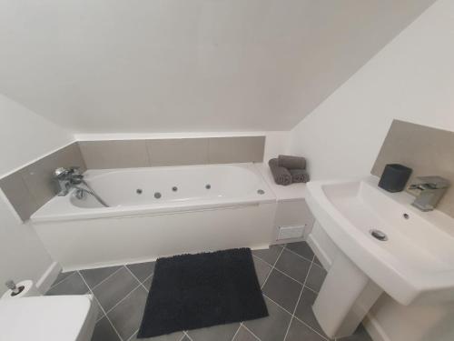 a white bathroom with a tub and a sink at Luxury 5 - Spacious Contractor's Delight with 4 Bedrooms and Ample Driveway Parking in Luton