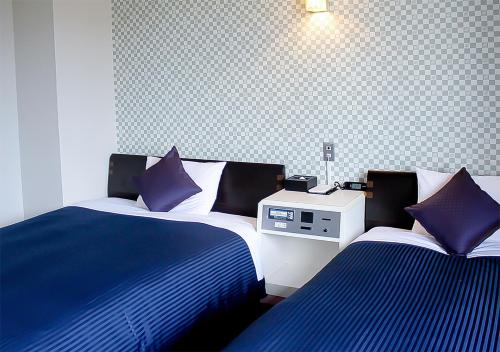 a bedroom with two beds with blue and white sheets at Hotel Livemax BUDGET Kanazawa-Idaimae in Uchinada