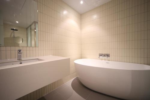 ein weißes Badezimmer mit einer Badewanne und einem Waschbecken in der Unterkunft Hound Hotel Junggwan in Busan