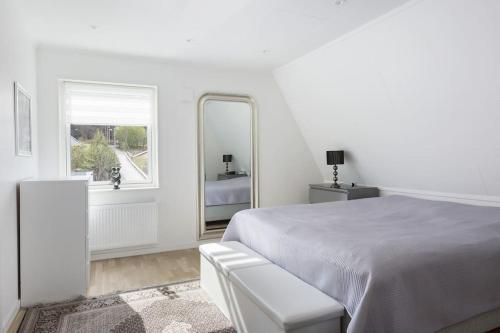 a white bedroom with a bed and a mirror at Modernt hus med parkeringsplatser och trädgård in Gothenburg