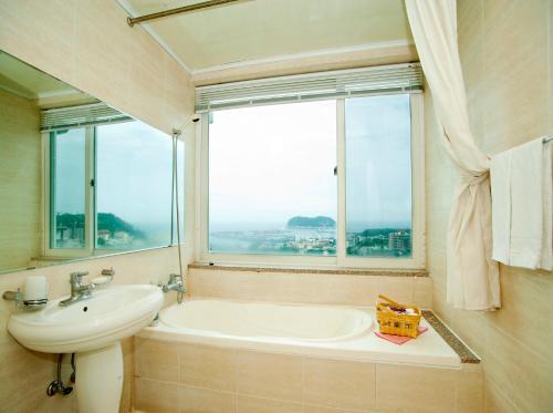 ein Bad mit einer Badewanne, einem Waschbecken und einem Fenster in der Unterkunft Hotel Good Inn in Seogwipo