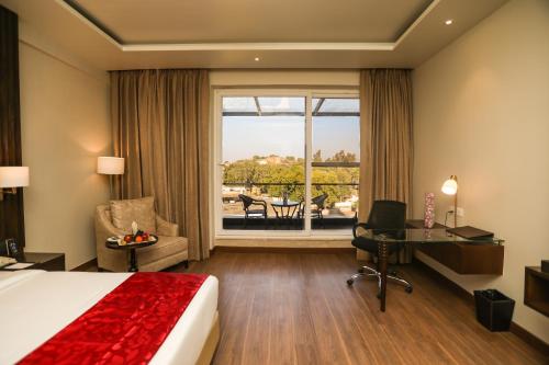a hotel room with a bed and a desk and a window at Regenta Place Jhansi by Royal Orchid Hotels Limited in Jhānsi