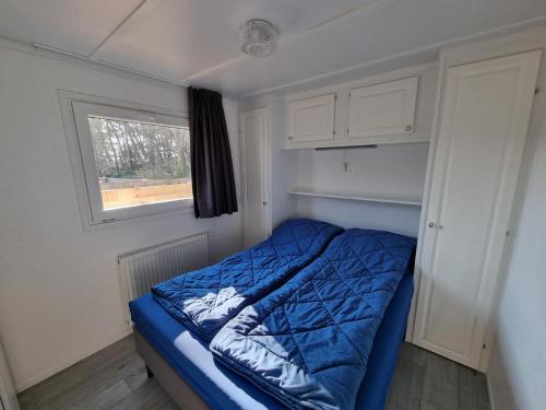 a small bedroom with a blue bed with a window at Chalet Texel DREaM nr. 17 op Chaletpark Bregkoog in De Koog