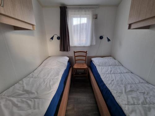 2 Betten in einem Zimmer mit einem Stuhl und einem Fenster in der Unterkunft Chalet MaMaMia nr. 54 op Chaletpark Bregkoog in De Koog