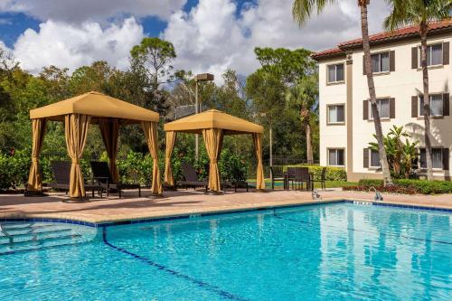 a swimming pool with chairs and umbrellas next to a building at Hawthorn Suites by Wyndham Naples in Naples