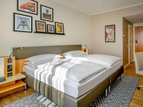 uma cama grande num quarto com fotografias na parede em Mercure Hotel Bochum City em Bochum