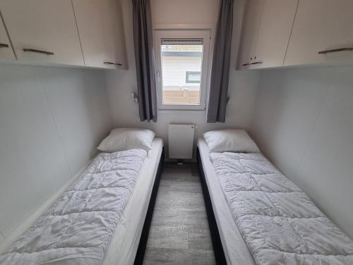 two beds in a small room with a window at Chalet 82 op Chaletpark Bregkoog in De Koog