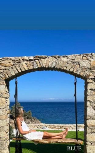 a woman sitting on a swing near the ocean at Toxotis Villas in Armenistis