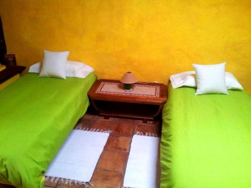 two beds with green sheets and a table between them at El Drago Rural House in Alajeró