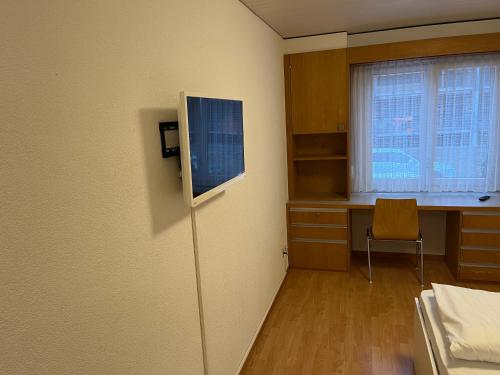 um quarto com uma televisão, uma secretária e uma janela em HoStel Self Check-In Solothurn em Zuchwil