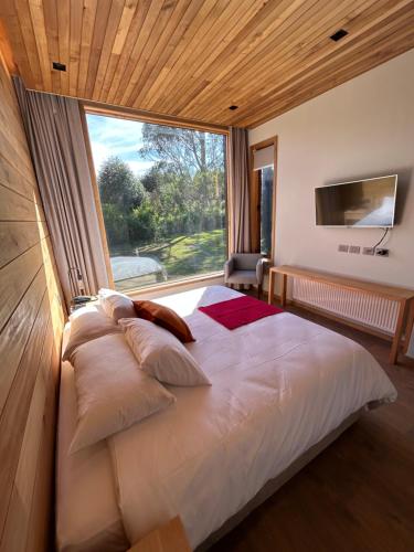 Cama grande en habitación con ventana grande en Mawün Lodge, en Villarrica