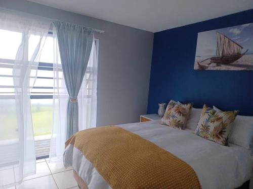 Schlafzimmer mit einem Bett mit blauen Wänden und einem Fenster in der Unterkunft ikhay'olwandle in East London