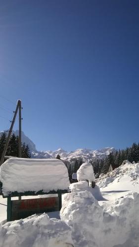 a bench covered in snow next to a pile of snow at Rooms Apartment Durmitor in Žabljak