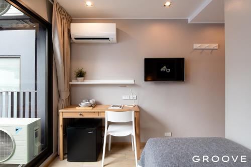 Habitación pequeña con escritorio y TV en la pared. en GROOVE AT SIAM en Pom Prap