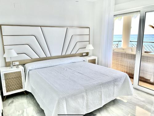 Dormitorio blanco con cama y vistas al océano en MI CAPRICHO 172 Beachfront Apartment, en Sitio de Calahonda