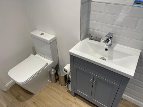 La salle de bains est pourvue d'un lavabo blanc et de toilettes. dans l'établissement Blackbird Cottage, à Kettering