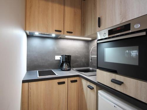 une cuisine avec des armoires en bois et un micro-ondes noir dans l'établissement Mont-Dore: T2 avec Balcon, Parking Couvert, 4 pers. - FR-1-608-109, à Le Mont-Dore