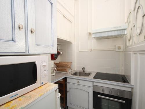 une cuisine avec des armoires blanches, un évier et un micro-ondes dans l'établissement Appartement lumineux T2 avec kitchenette équipée, lave-linge et ascenseur - FR-1-608-108, à Le Mont-Dore