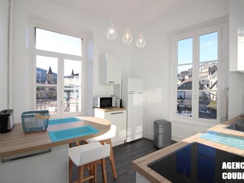 - une cuisine blanche avec une table et quelques fenêtres dans l'établissement LA BOURBOULE CENTRE - Beau T2 rénové, wifi et cuisine équipée - FR-1-608-159, à La Bourboule