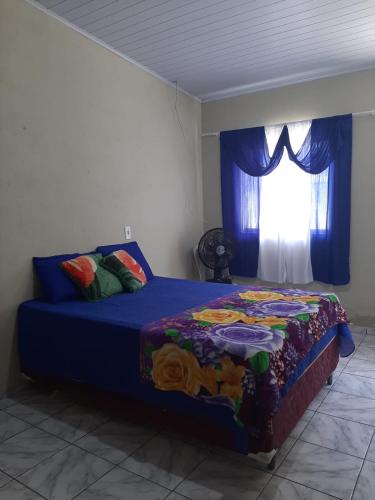 a bedroom with a bed with a blue comforter and a window at Pousada Recanto do Galo in Santa Cruz Cabrália