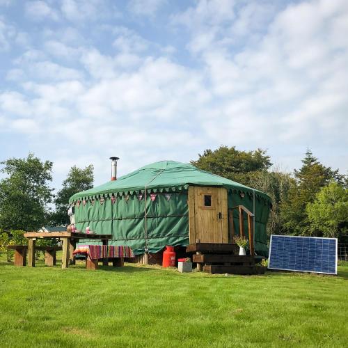 a green yurt in a field with a table and a solar panel at 'Villager' the Yurt at Pentref Luxury Camping in Penuwch