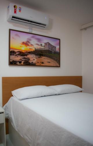 a bedroom with a white bed with a picture on the wall at POUSADA PEDRA DE JACÓ in Lauro de Freitas