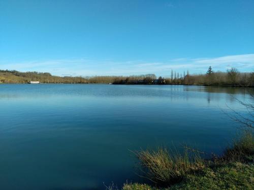 a large body of blue water with trees in the background at Le petit jazz du lac in Marciac