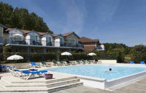 a pool at a resort with chairs and a building at Le petit jazz du lac in Marciac
