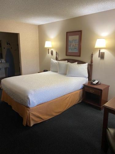 una camera d'albergo con un grande letto con lenzuola e cuscini bianchi di AmeriCoast Inn a Brookings