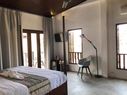 a bedroom with a bed and a chair and windows at Moonlight Champa Riverview in Luang Prabang