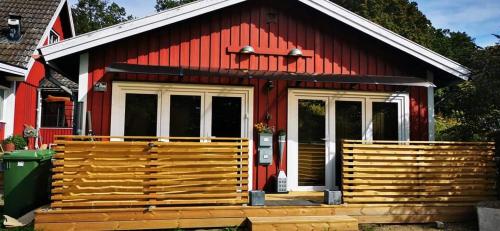 a red house with a large wooden porch at ÖLJERSJÖ COTTAGE in Lyckeby