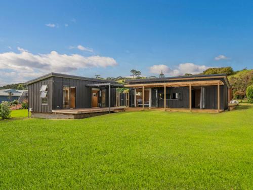 a black house with a large green yard at The Little Bach at Whangapoua in Whangapoua