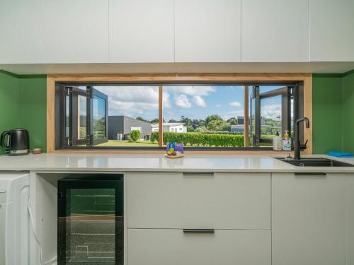 a kitchen with a window over a kitchen counter at The Little Bach at Whangapoua in Whangapoua