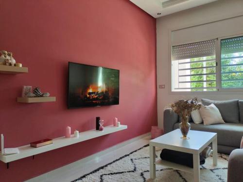 a living room with a red wall with a tv at Cosy appartement à proximité de l'aéroport de salé et technopolis in Oulad Yakoub