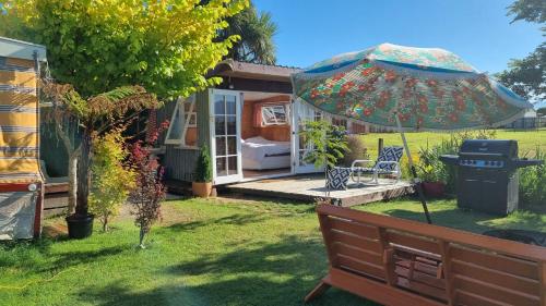 韋斯特波特的住宿－Delightful 1 bedroom tiny house, with retro Poptop，花园设有长凳、遮阳伞和烧烤架。
