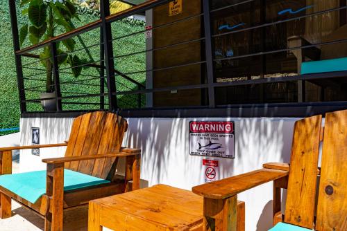 two wooden chairs and a warning sign in front of a building at Shark Town Mal Pais in Santa Teresa Beach
