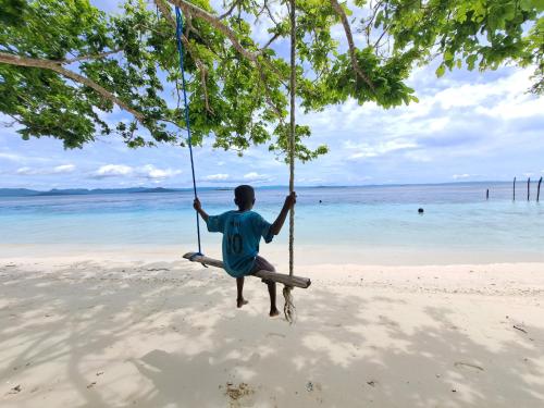 a man sitting on a swing on the beach at Raja Ampat Jousuba Homestay in Minyaifuin