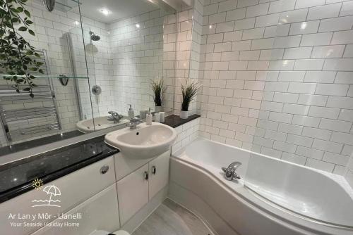 a white bathroom with a sink and a tub and a sink at Ar Lan Y Mor - Stunning 2 bed coastal apartment in Llanelli